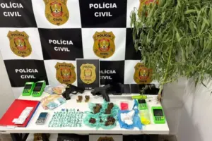 Drogas, armas, munições, celulares e balanças sobre uma mesa diante de painel da Polícia Civil do DF