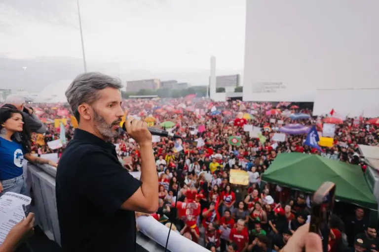 Leandro Grass fala ao microfone diante de participantes de um ato público.