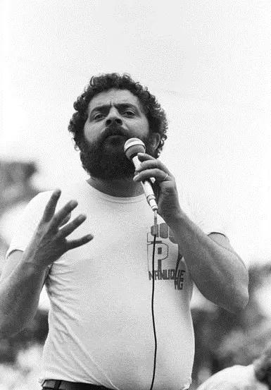 Lula jovem discursa ao microfone em 1982, usando camiseta do PT