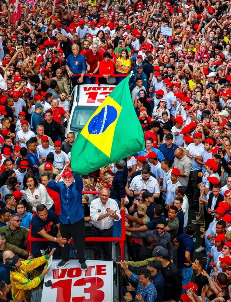 Lula agita a bandeira do Brasil sobre um carro, cercado por apoiadores na Avenida Paulista.