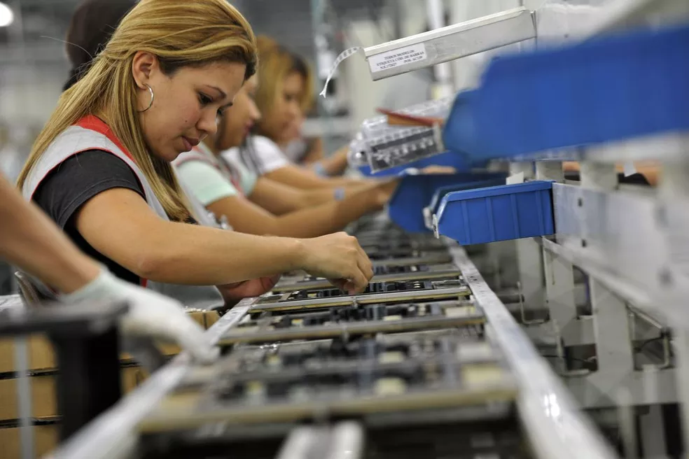 Mulheres trabalham em uma linha de montagem industrial.